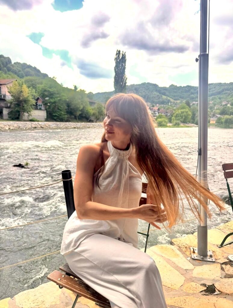 Galina Maslovska, svjetska šampionka u bikini fitnessu, sjedi na terasi kraj rijeke Vrbasa u Banjaluci tokom intervjua. Nasmijana je, gleda u stranu i rukom popravlja dugu, svijetlosmeđu kosu koja vijori na vjetru. Nosi elegantan bijeli top s halter ovratnikom i bijele pantalone. U pozadini je rijeka Vrbas, šumovito brdo i kuće.